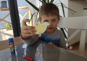 dziecko siedzi przy stole i pokazuje kurczaka z papieru
